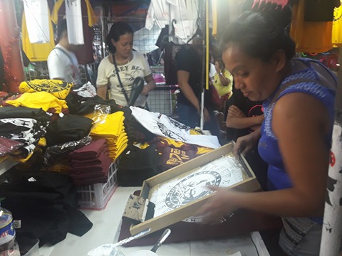 A woman vendor  in Carriedo street prints a t-shirt through silkscreen materials and sell them to the customers